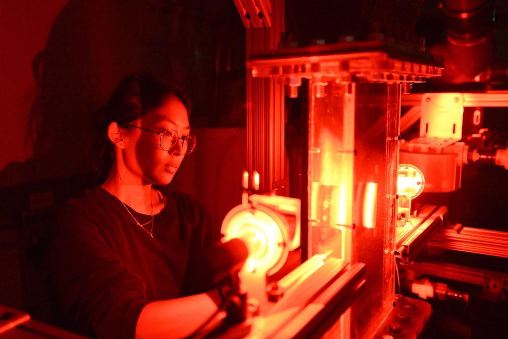 A student stands behind a glowing red machine.