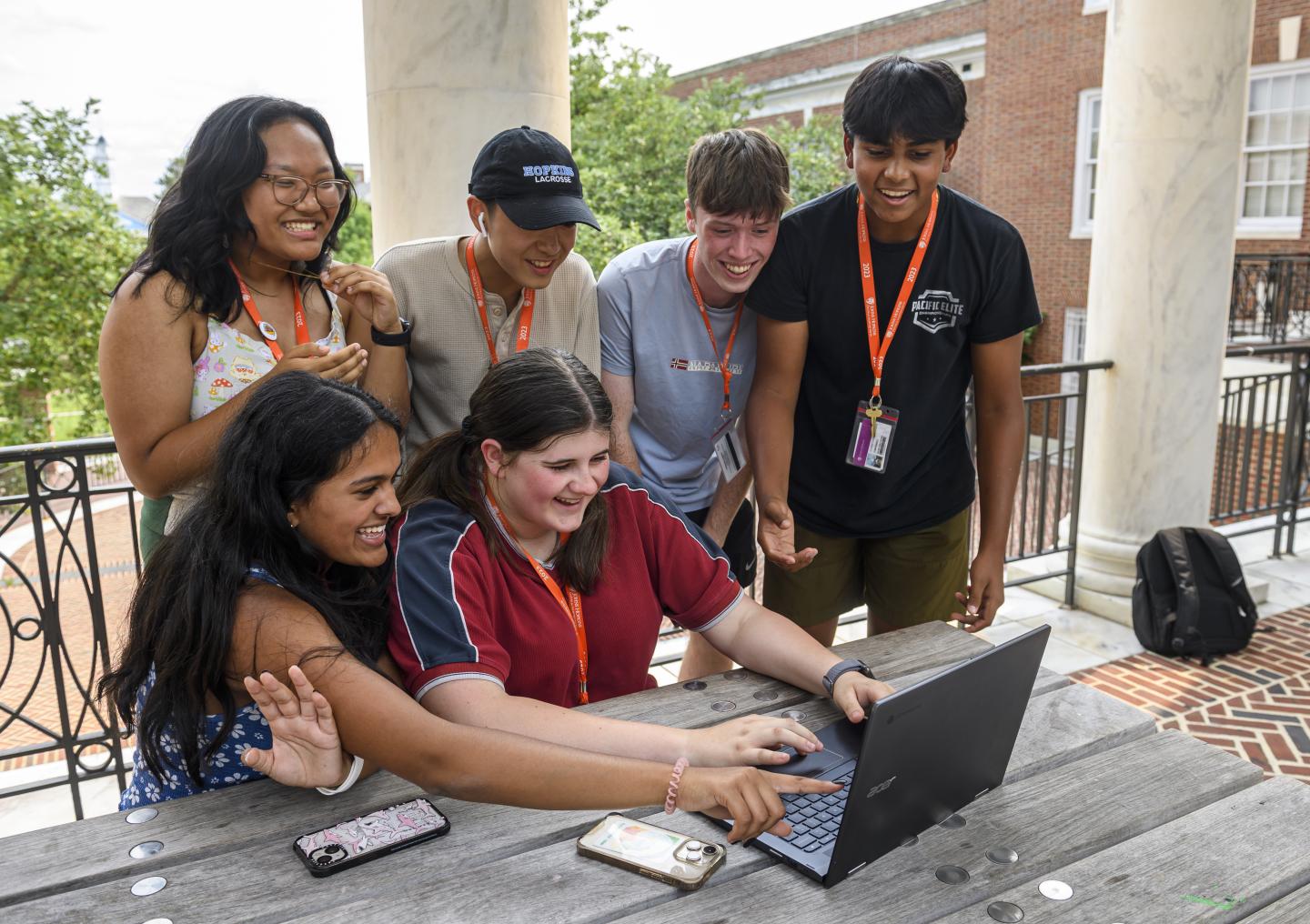 Six students smile as they look at a laptop screen.