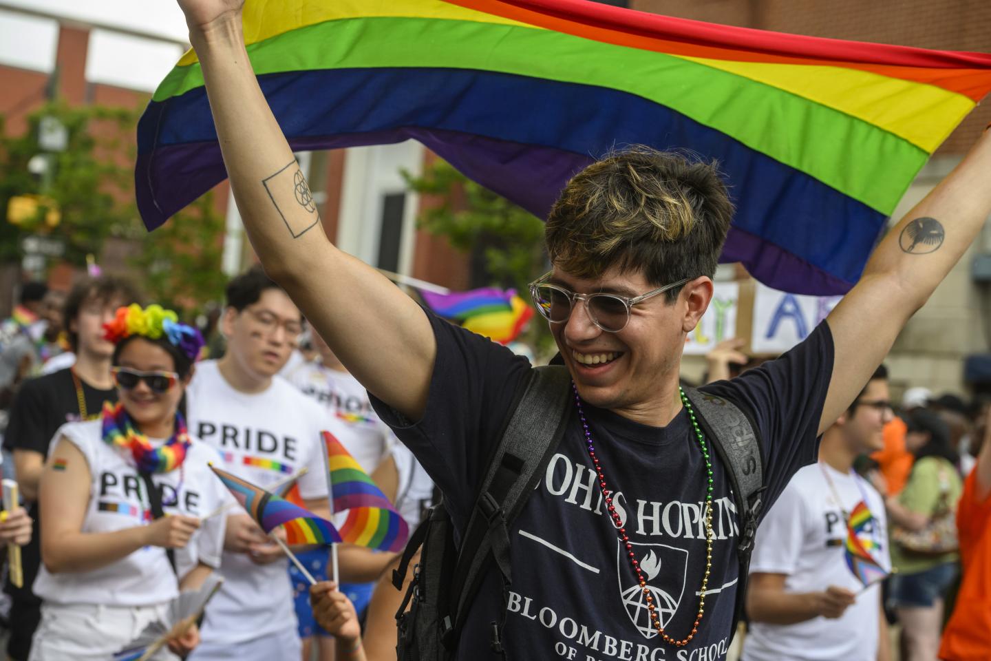An adult holding a rainbow flag walks in a pride parade.
