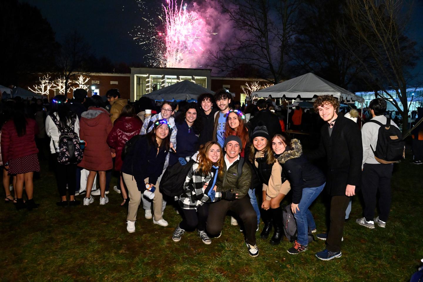 A group of students pose for a photo while fireworks burst in the background