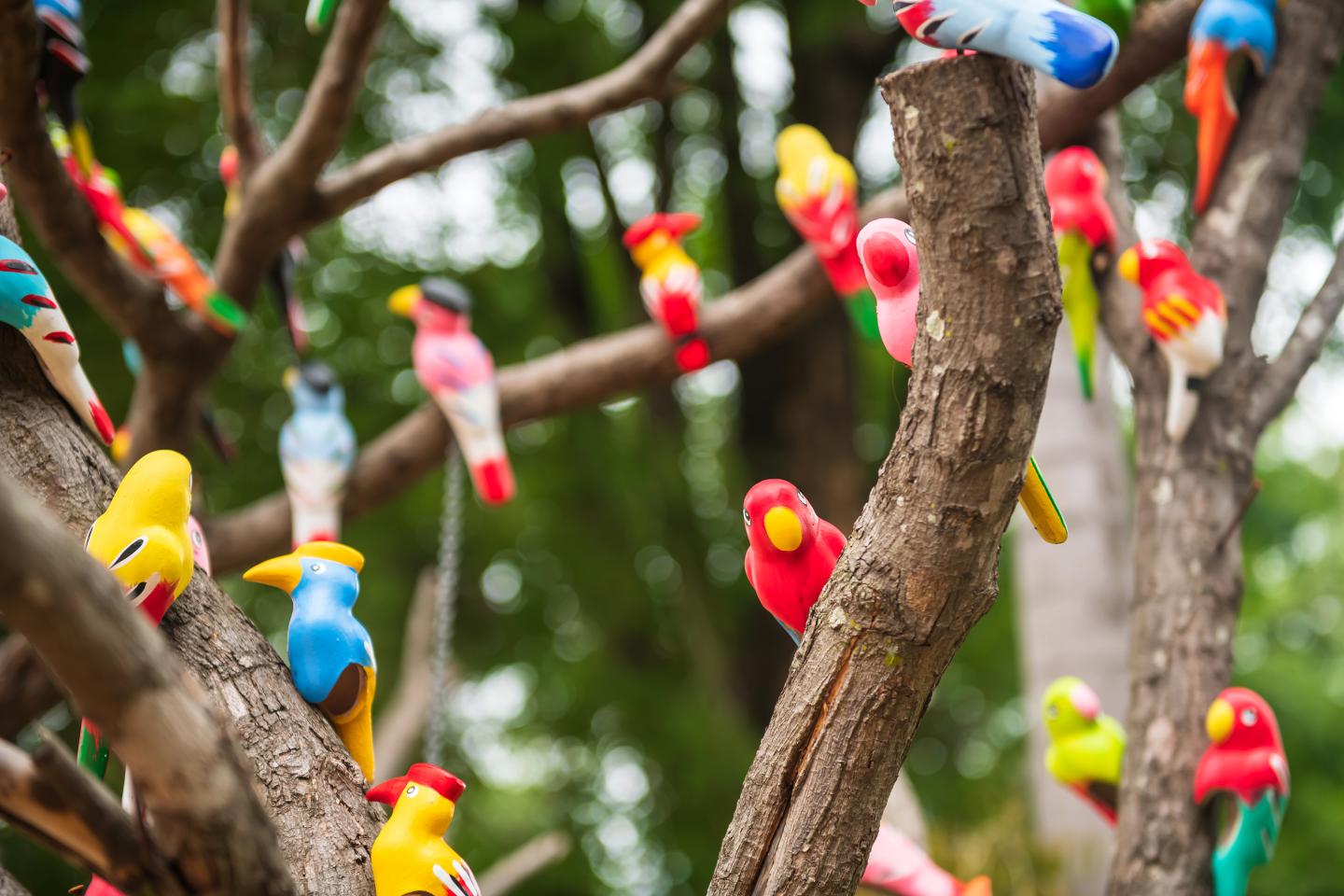 Fake colorful birds standing on tree with blur foliage bokeh
