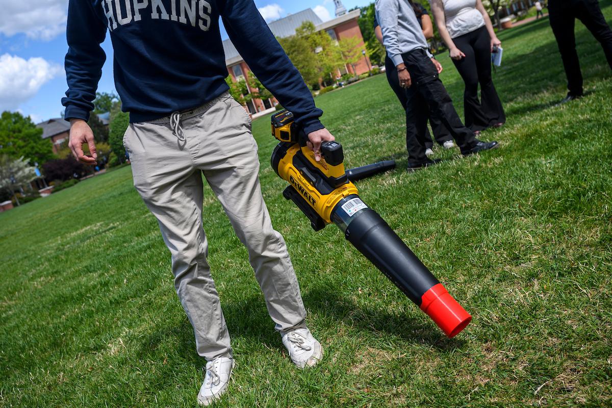 A student in a Hopkins sweatshirt demonstrates the quieter leaf blower