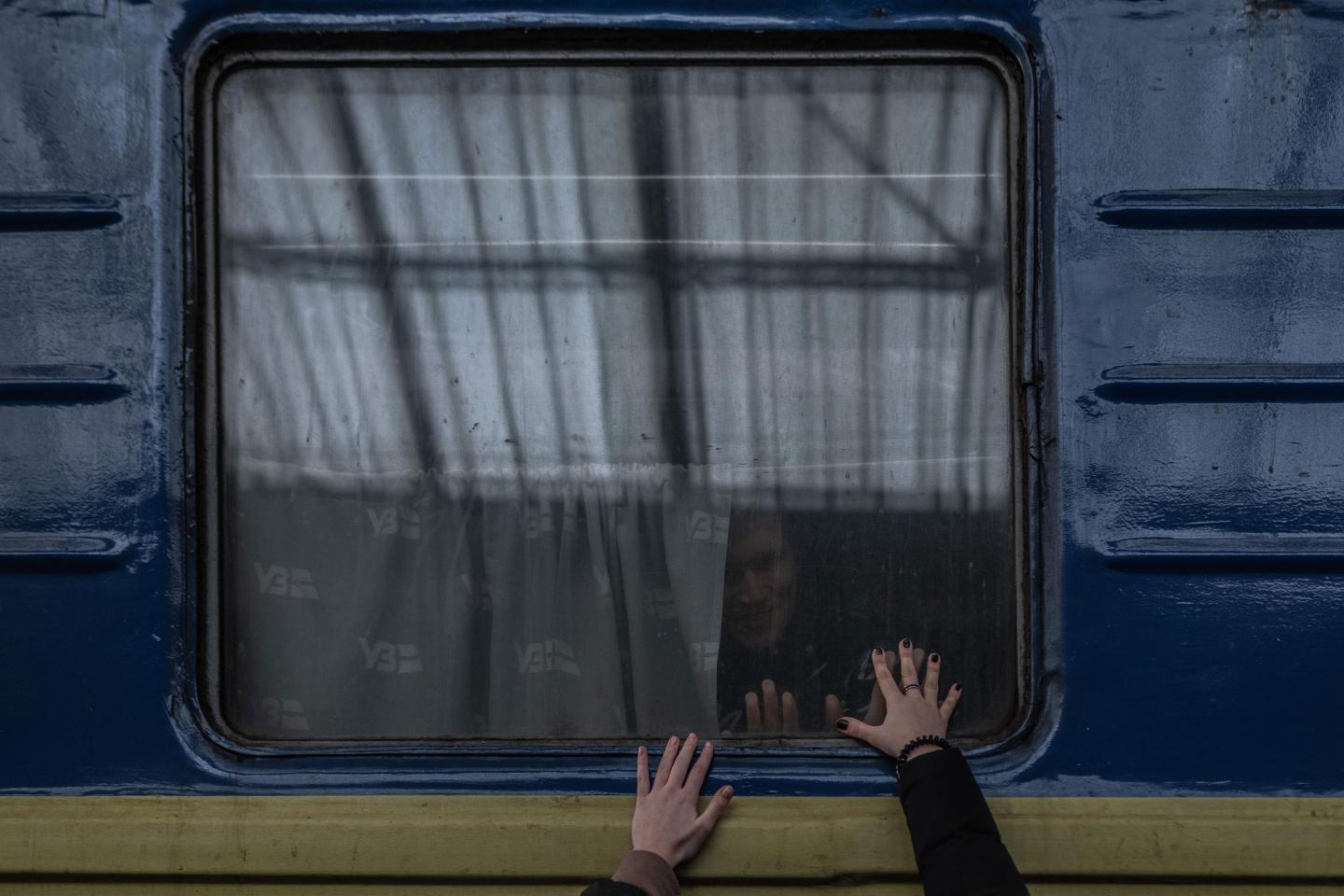 Two hands reach up to touch the window of a train leaving Lviv, Ukraine. Inside the train, a face looks out.