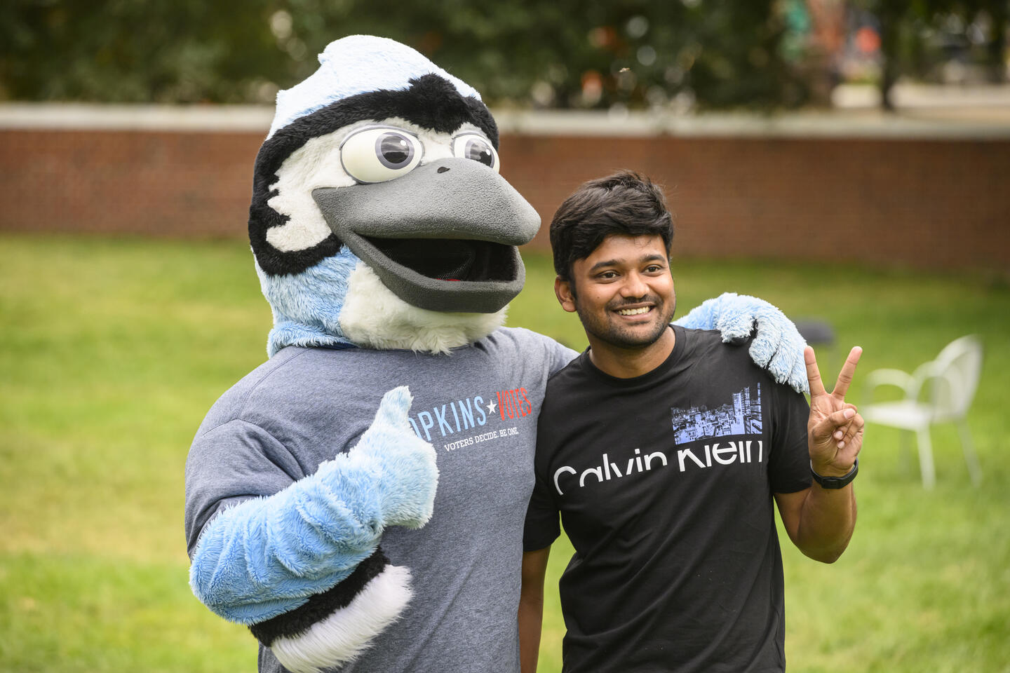 A student poses for a photo with Jay the Blue Jay Mascot. The student is making a peace sign and Jay is making a thumbs up.