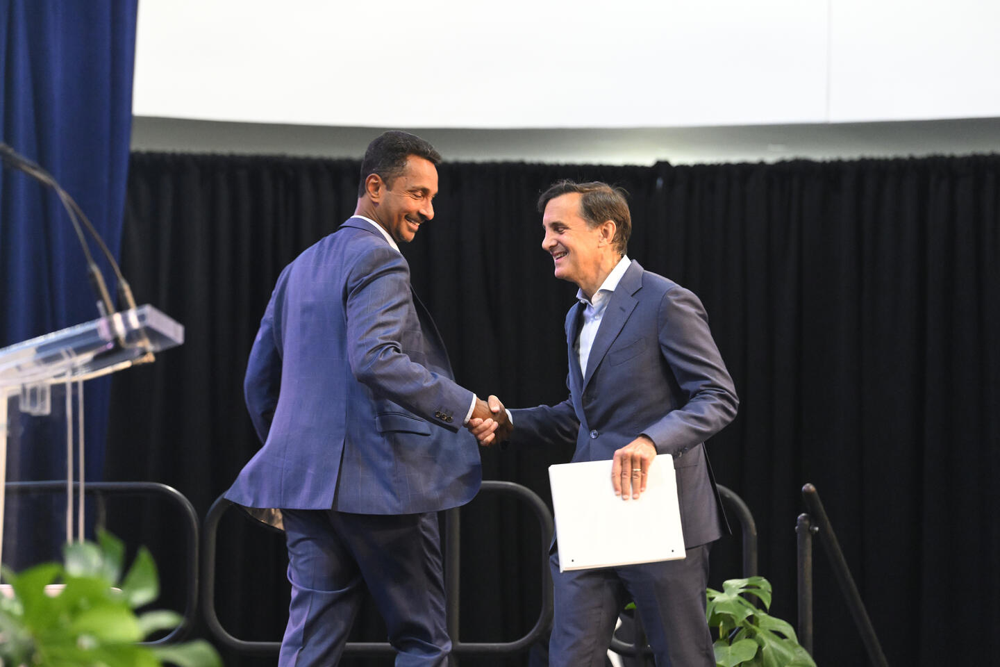 Provost Ray Jayawardhana and JHU President Ron Daniels shaking hands while passing each other on a stage near a podium