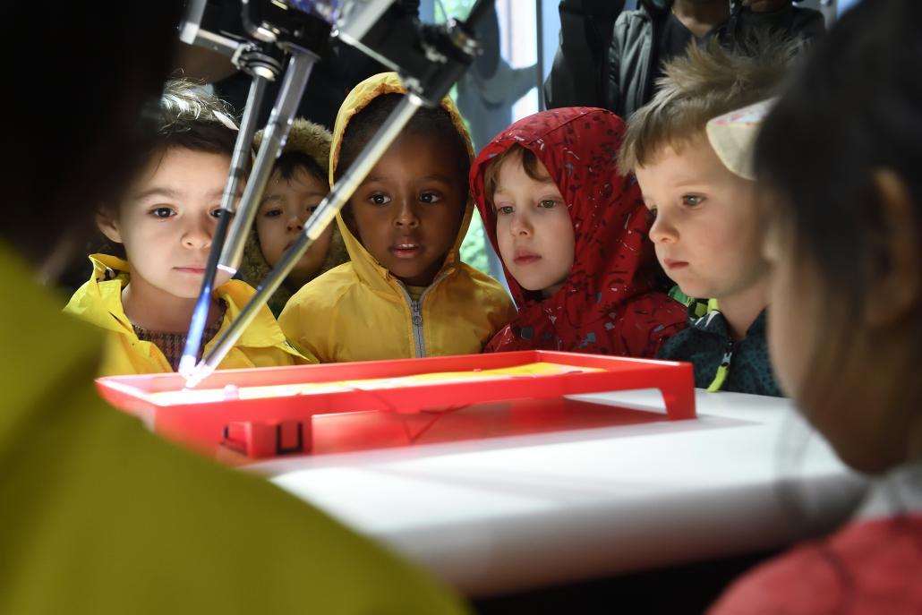 A group of kids watch as a surgical robot plays the board game Operation.