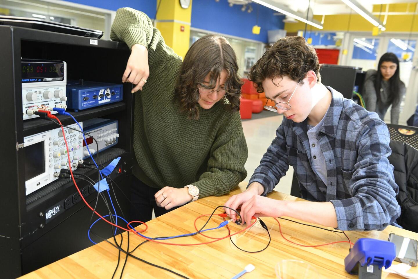 Two college students work attach electrical wires as part of a project.