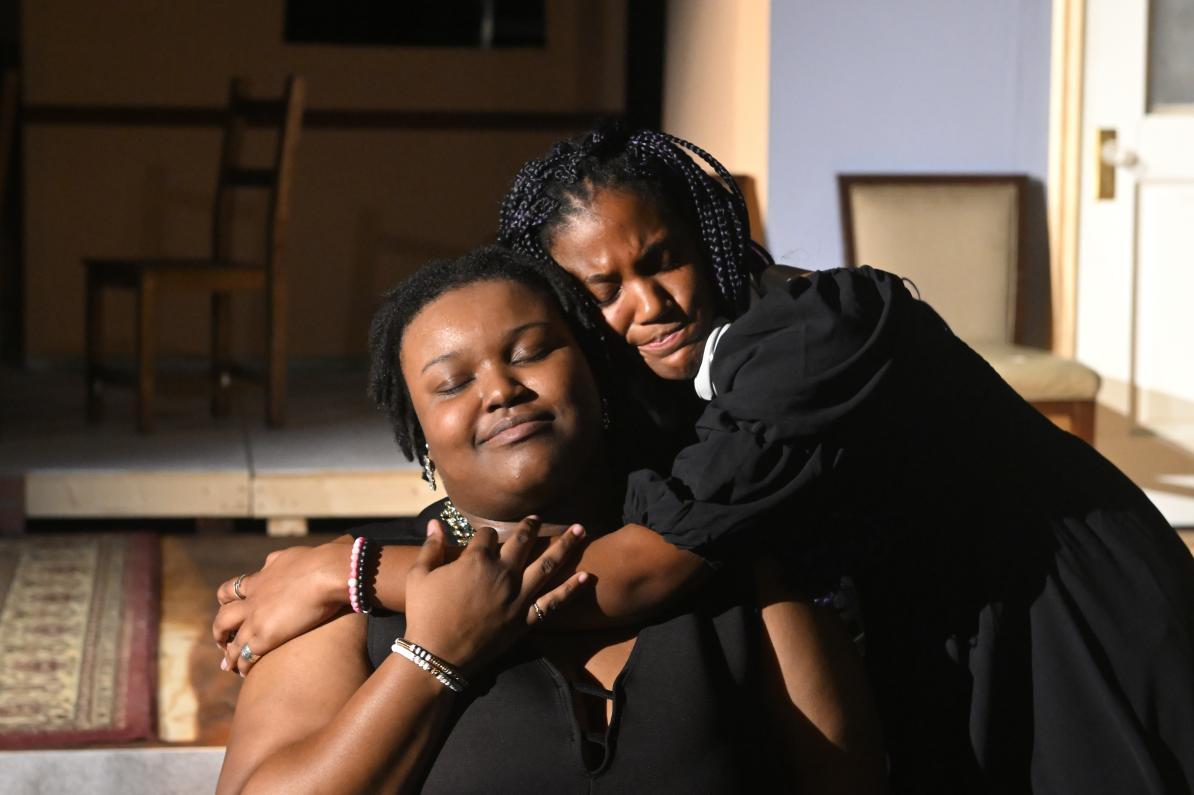 Two adults dressed in black give each other an emotional side-hug.