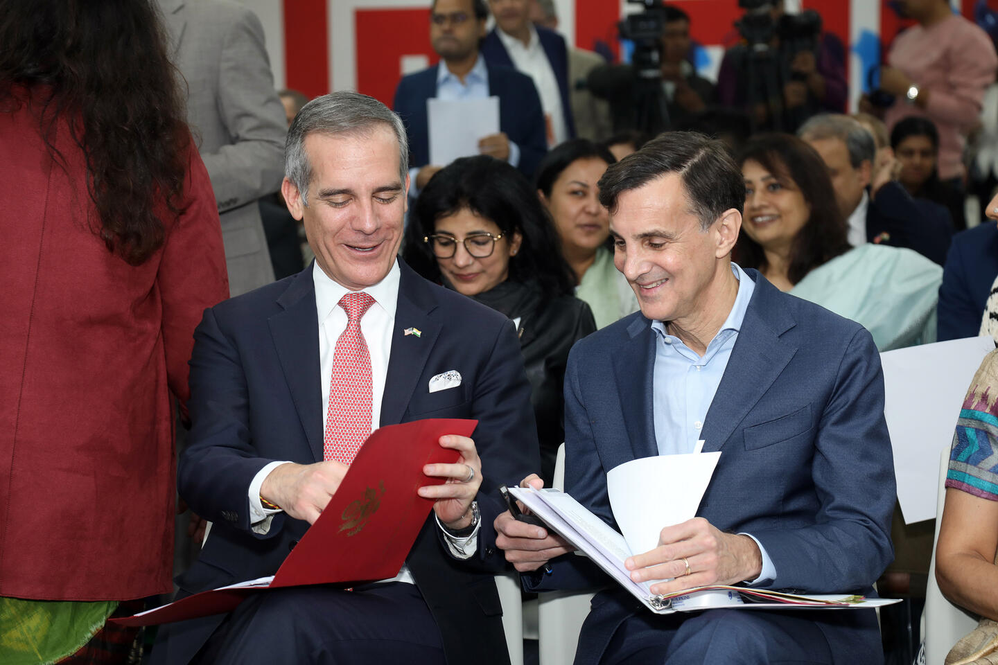 Two men seated next to each other look at notes in binders