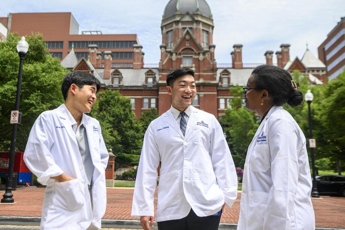 Three medical students wearing doctor's coats talk to each other outside on the Johns Hopkins Medical Campus.