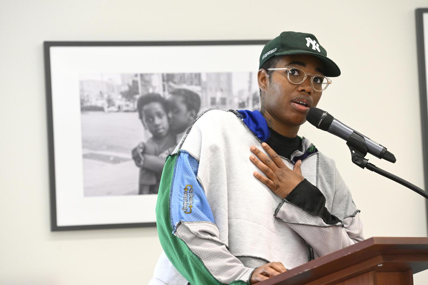 SHAN Wallace speaks into a microphone while standing in front of a black-and-white photograph of two young Black boys.