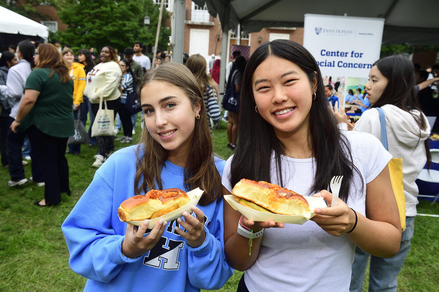 Two female students smile with plates of food outside on the quad