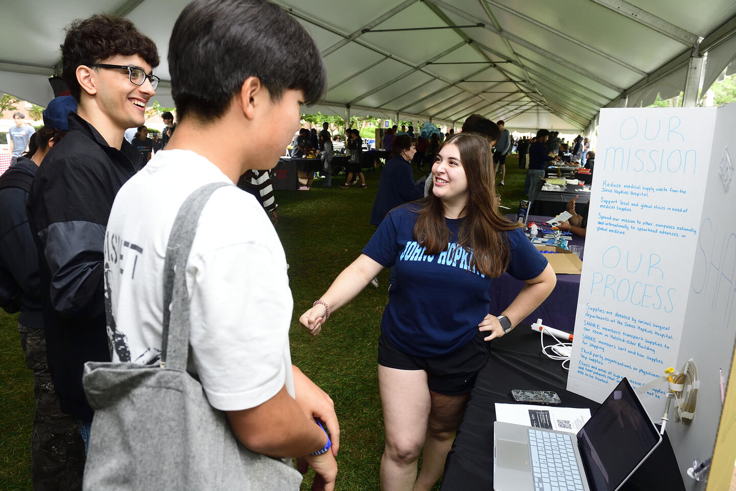 A female student running a booth talks to two male students about her student organization