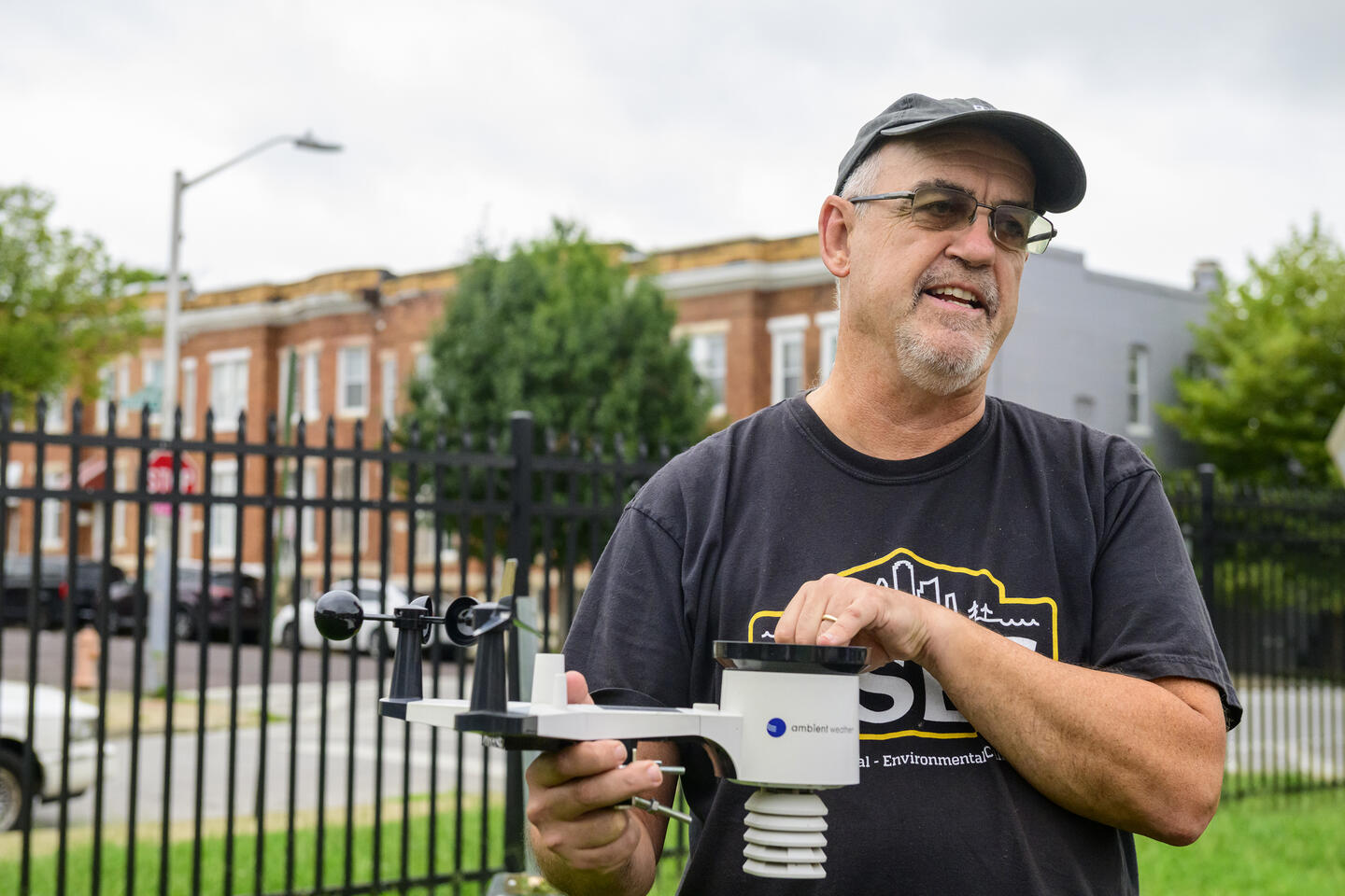 A man in a black t-shirt and glasses works with a weather monitoring device outside