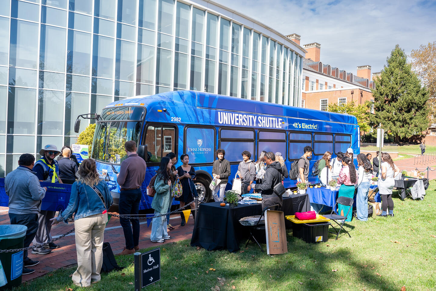 A small crowd of people gathers around a blue electric bus