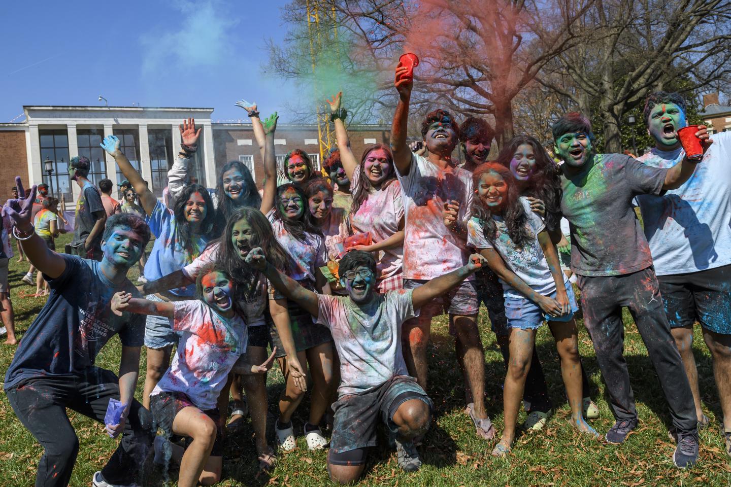 A group of college students covered in colorful powder throw more into the air.