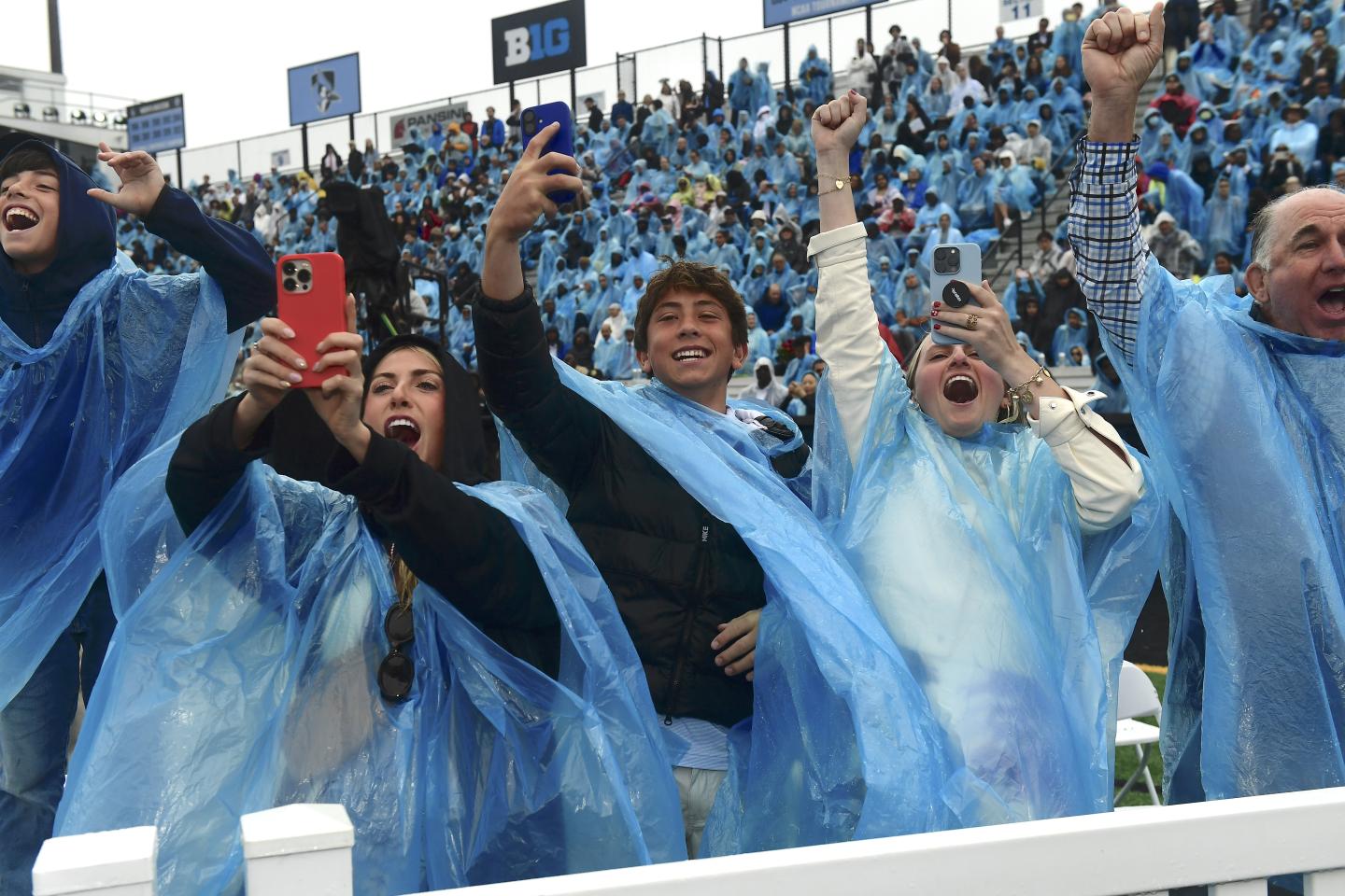 A crowd in matching blue rain ponchos cheers.