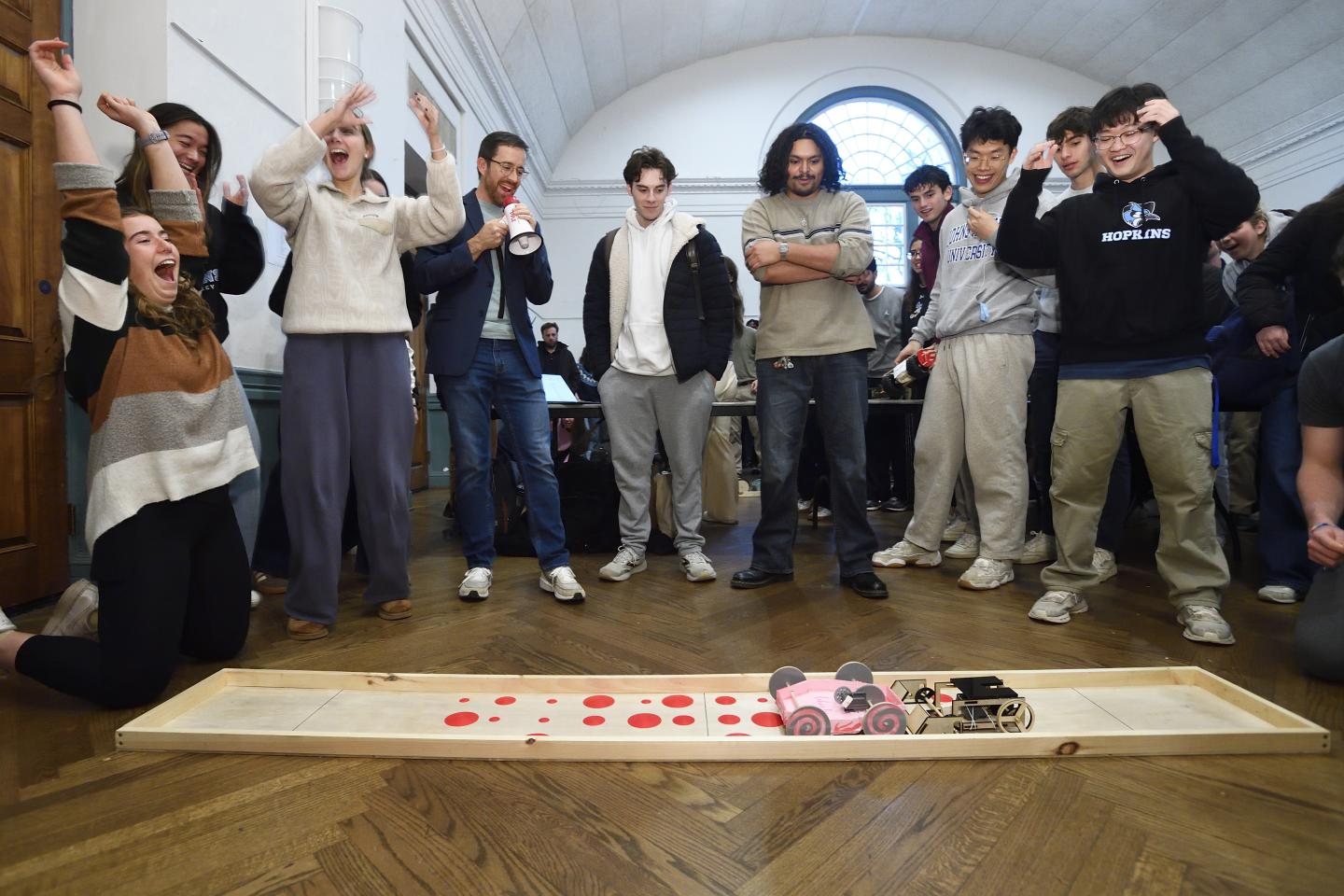 A group of people have mixed reactions at the outcome of a mechanical toy car competition where the vehicles tried to push each other.