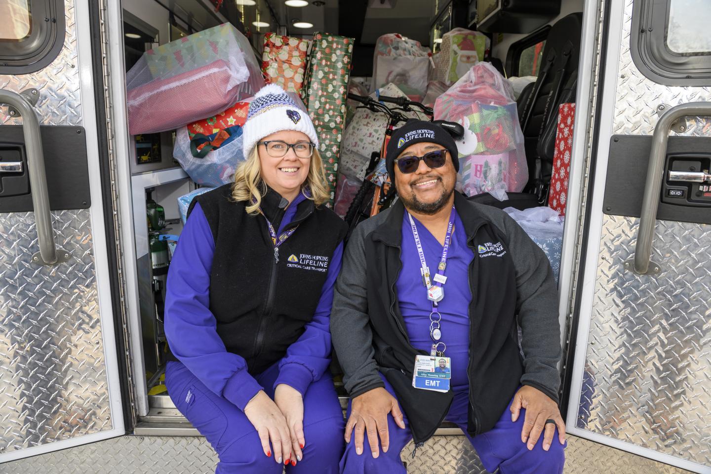 Johns Hopkins affiliates smile while sitting on the back of an ambulance full of gifts
