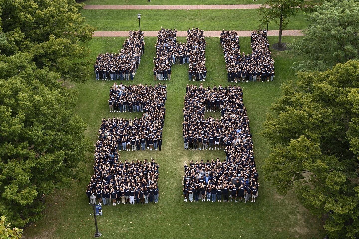 Hundreds of people wave at the camera while arranged to spell 