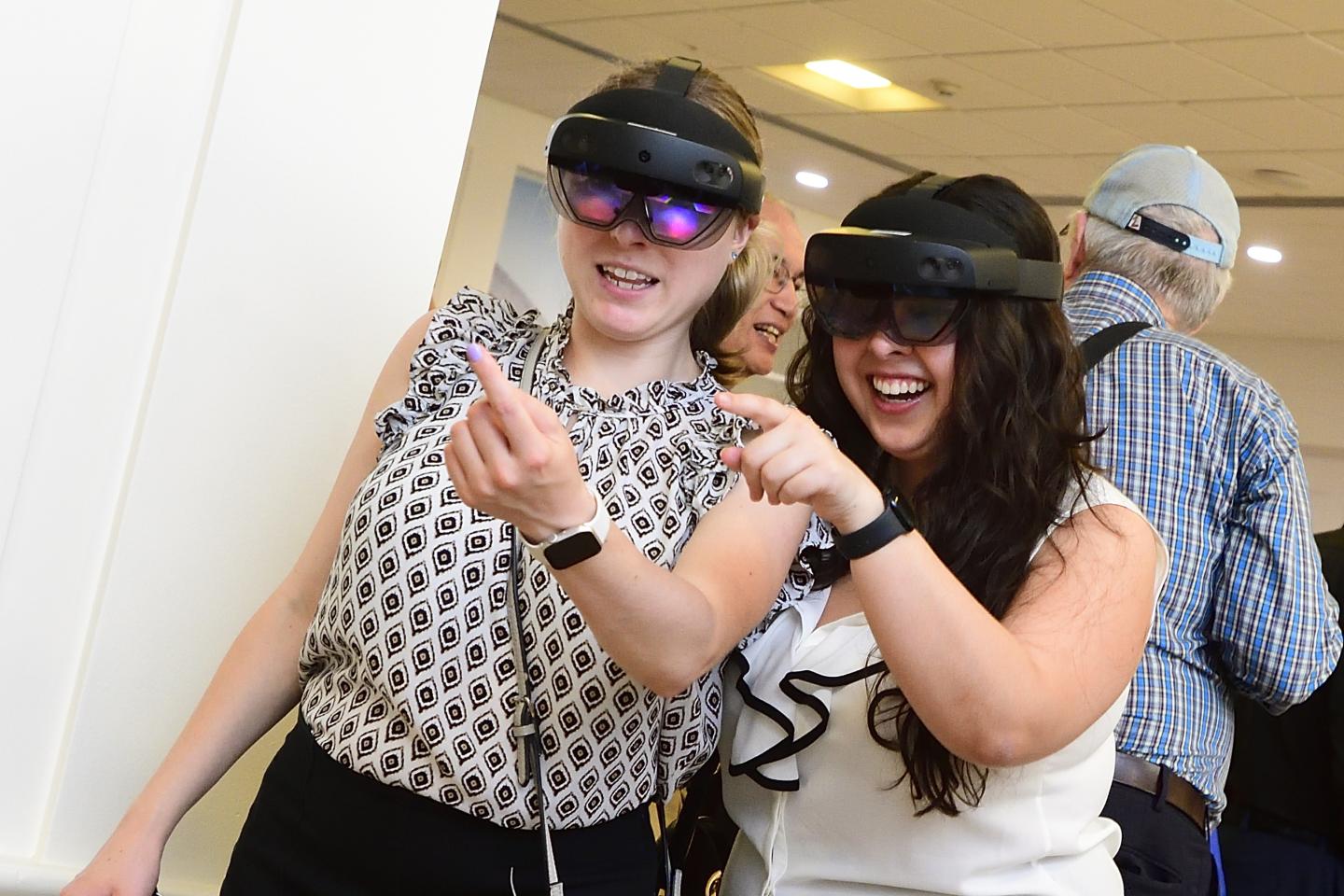 Two adults point at something while wearing VR headsets.