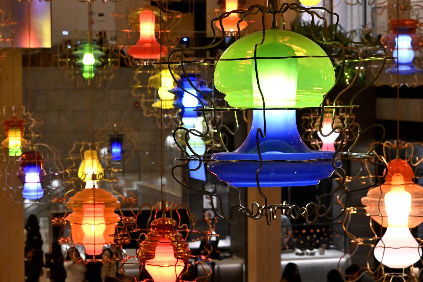 A variety of colorful, organic-shaped glass chandeliers hang from the ceiling.