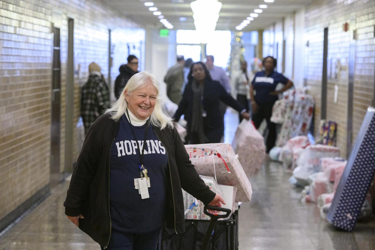 A Johns Hopkins affiliate smiles while pulling a wagon full of presents in the halls of JH at Eastern