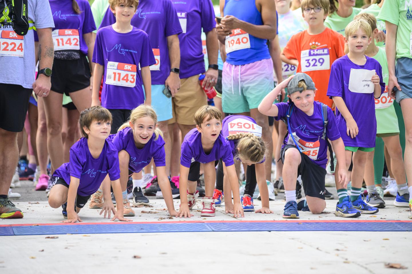 Children in matching purples shirt line up with their hands on the ground to run a 5k.