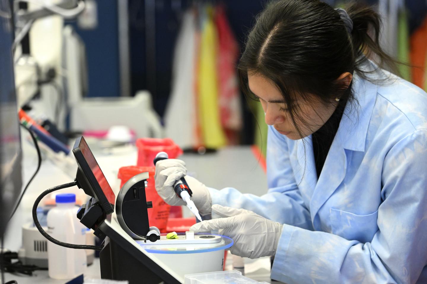 A scientist wearing a blue lab coat performs their work in a lab.
