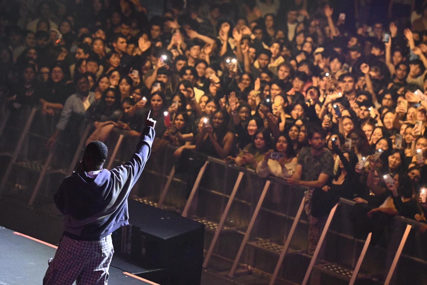Khalid points his finger in the air while singing into a microphone. In front of him is a crowd of fans.