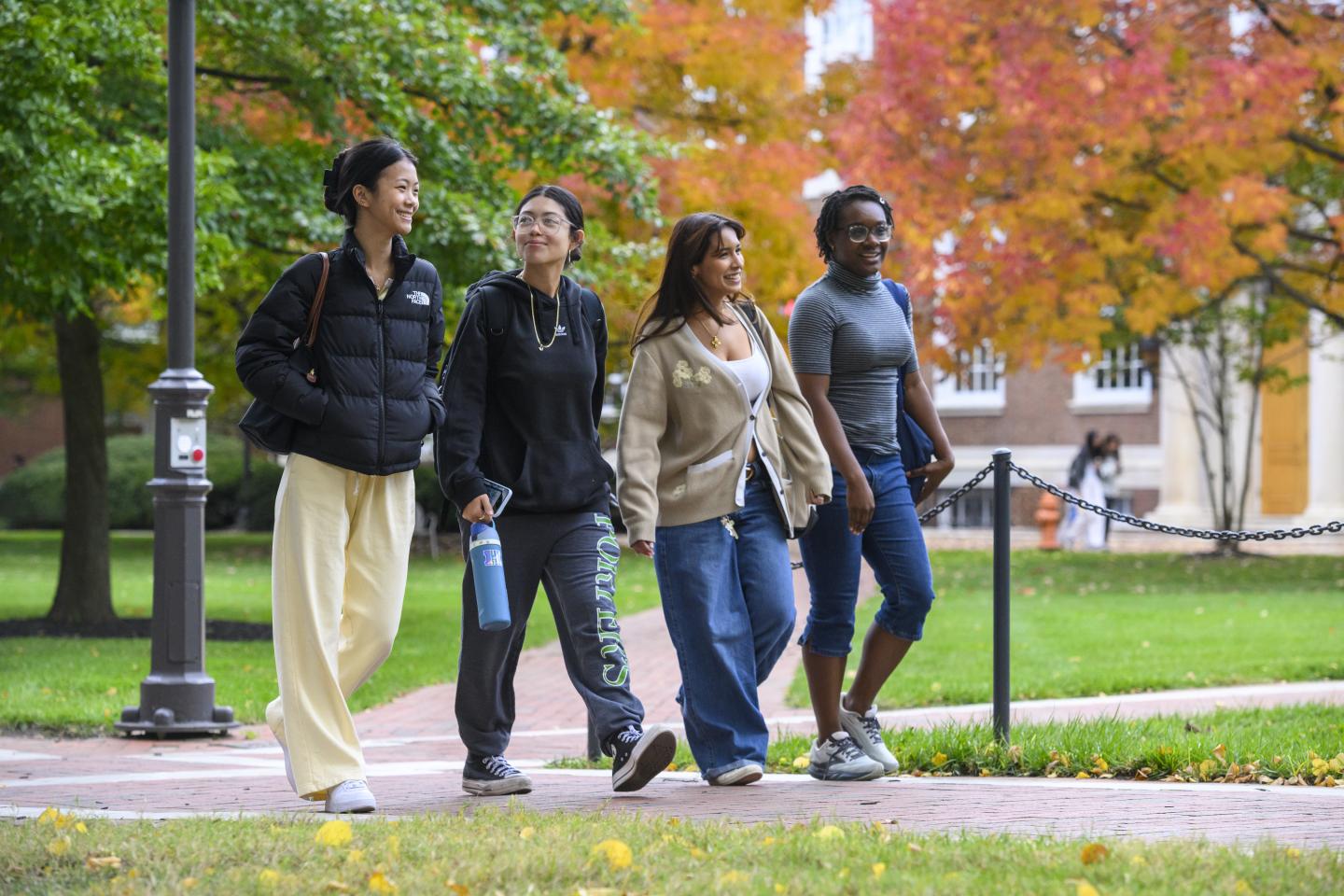 Four college students walk across Homewood campus on a fall day.
