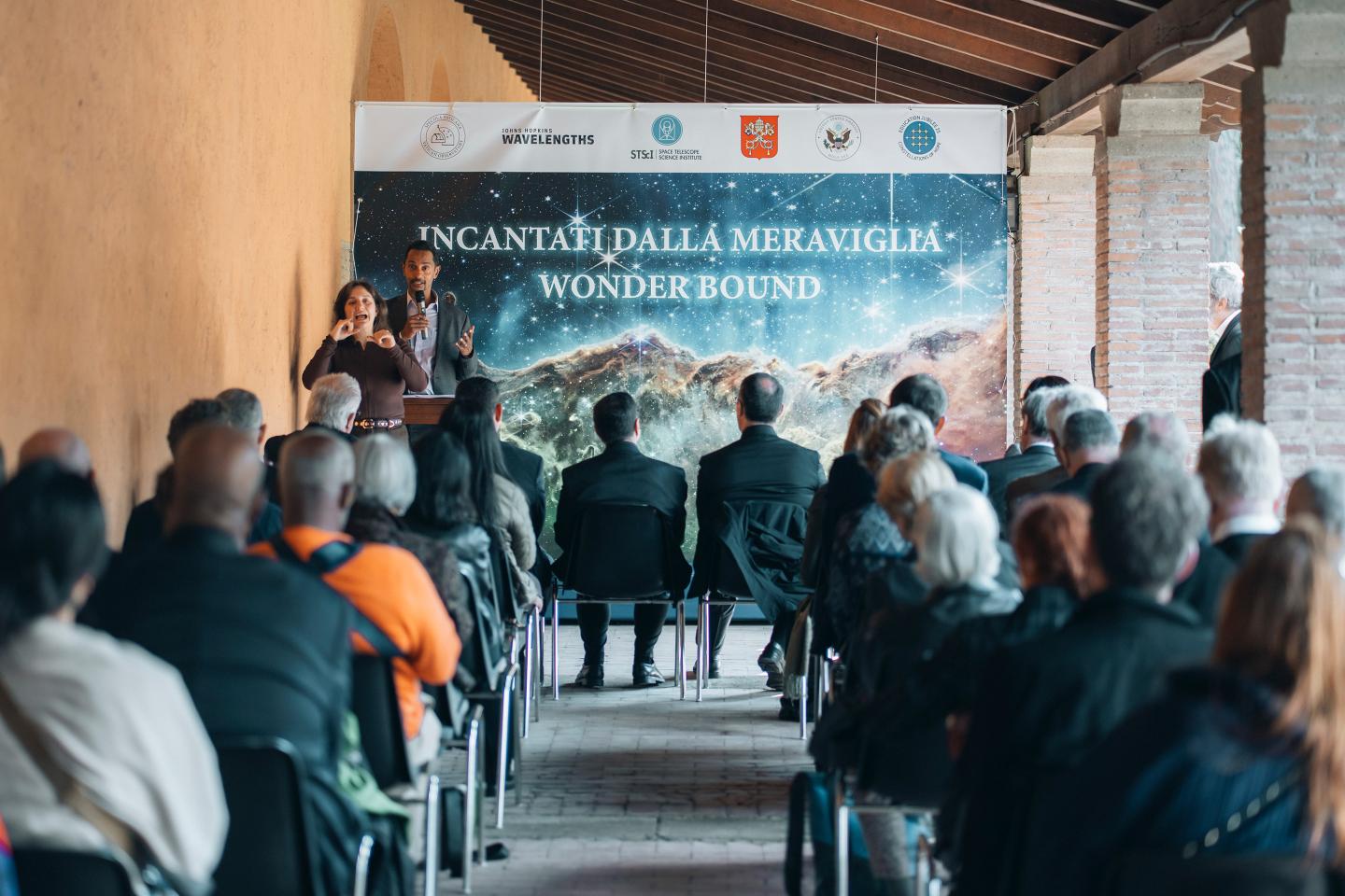 A man addresses a small crowd seated outside
