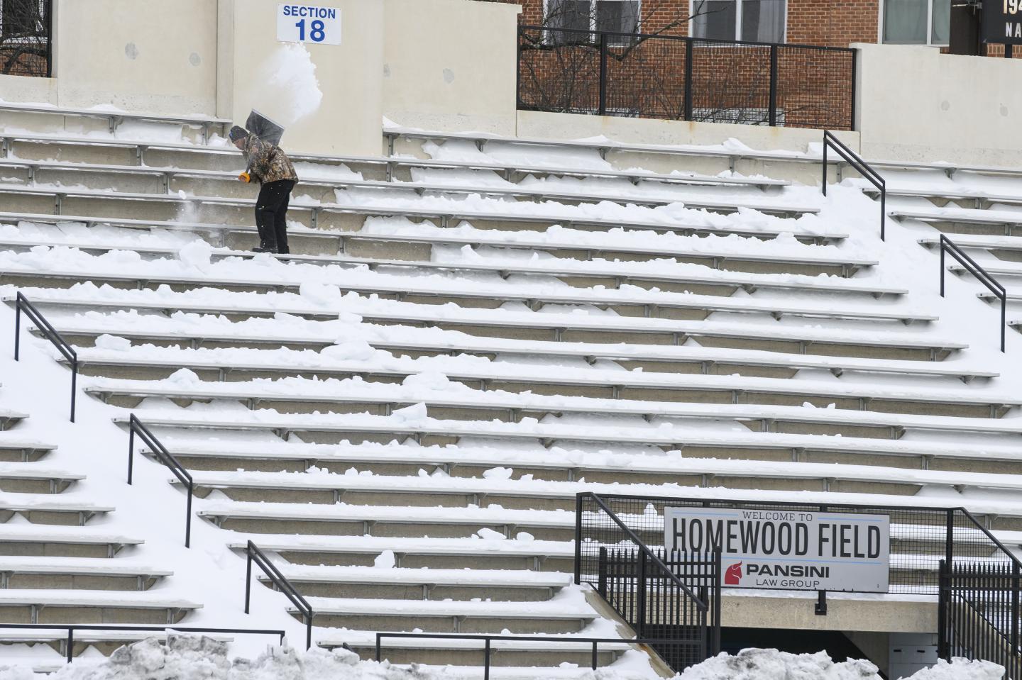 An athletics staff member shovels snow from the stands at Homewood Field