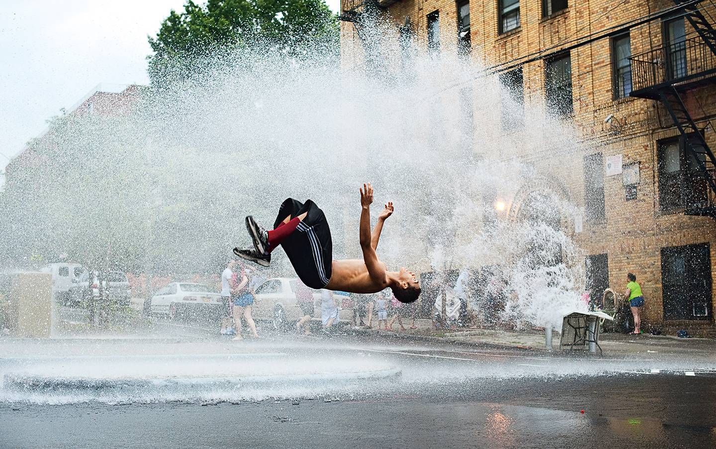 A man does a backflip in the spray of an open fire hydrant