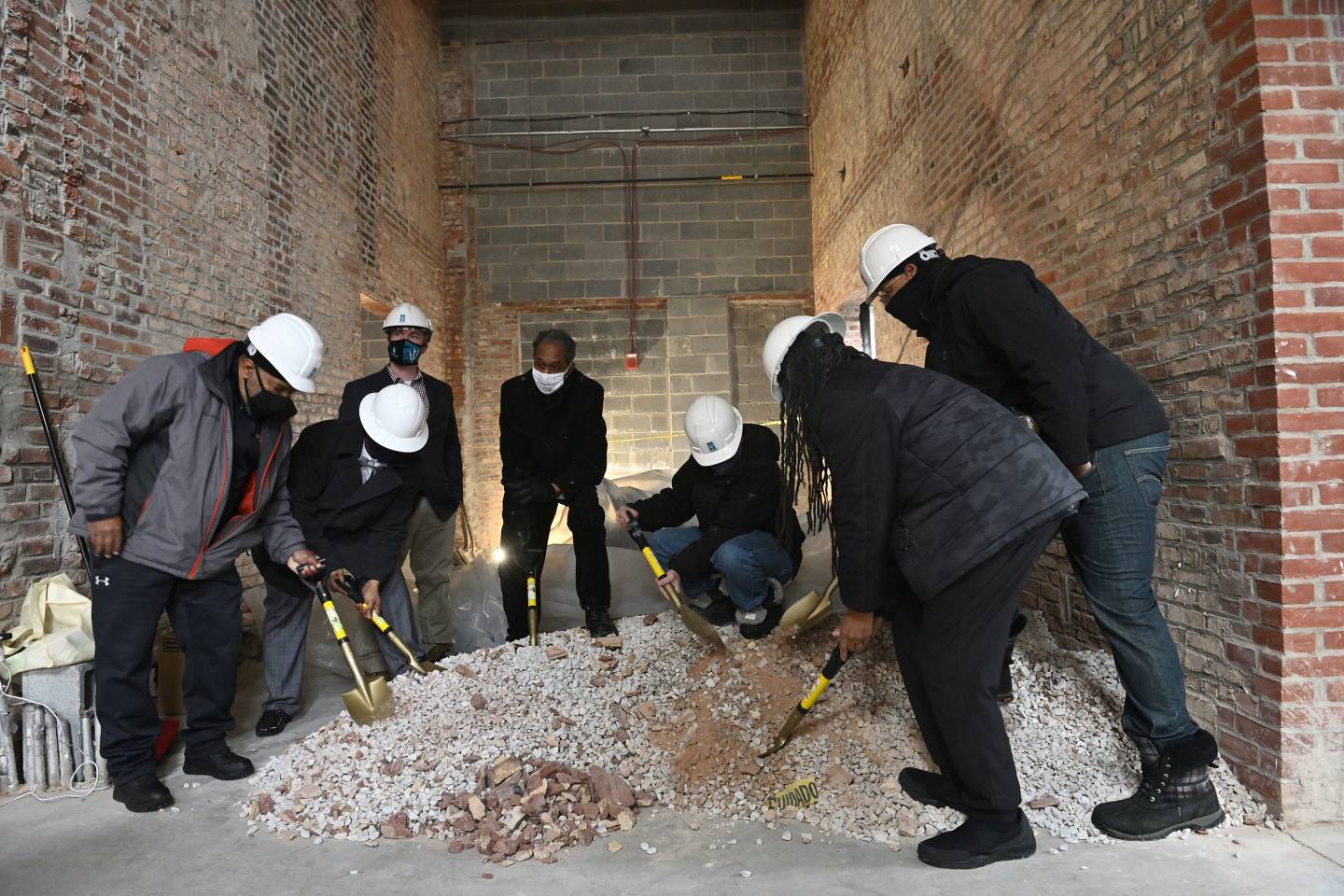 Community leaders and developers shovel brick dust in an empty row home