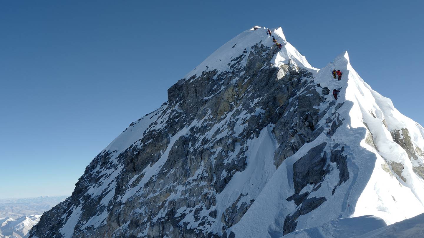 Climbers climb a mountain ridge over Everest Climbers climb a mountain ridge over Everest