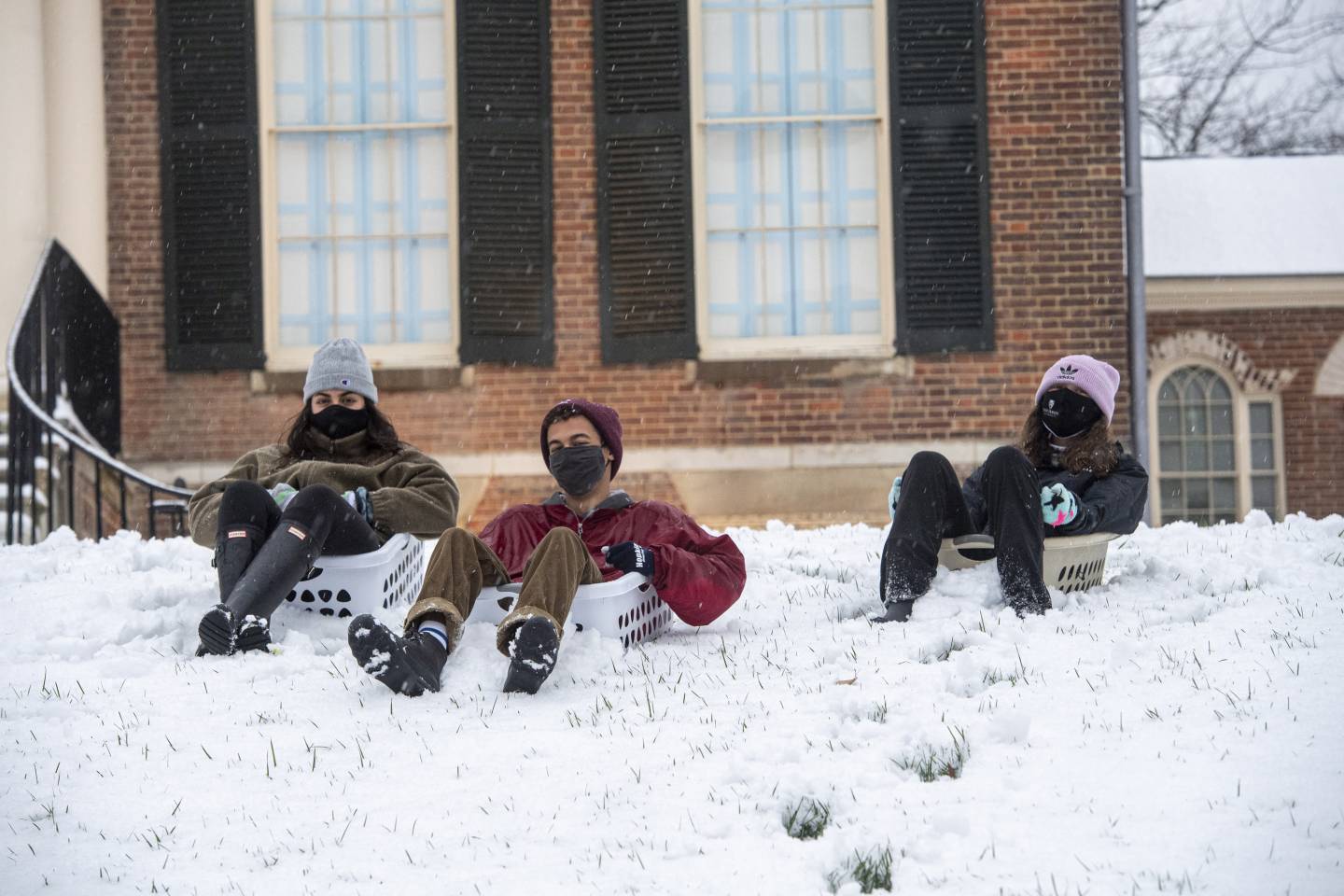 Three masked students sit in laundry baskets in the snow