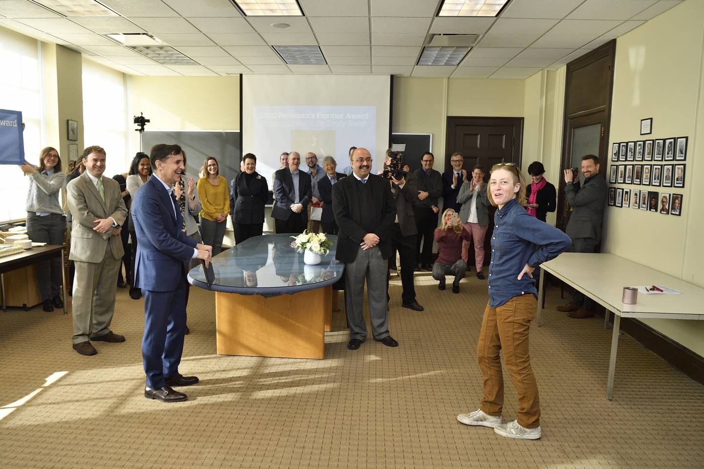 Emily Riehl looks to the camera in surprise as a group of her colleagues surprise her with an award