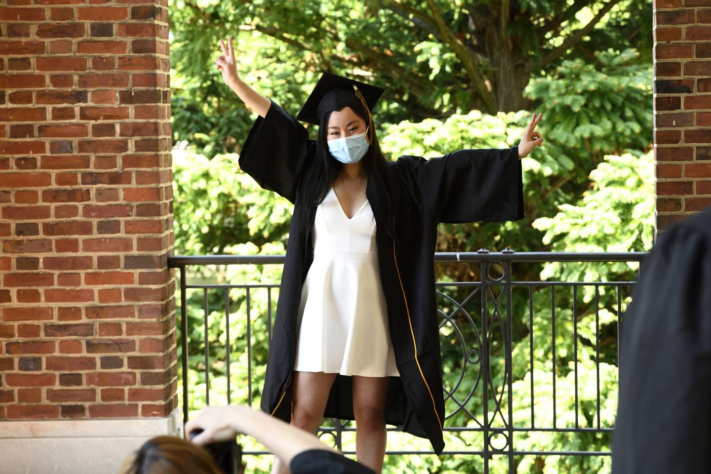 A student in cap and gown and a mask poses for a photo