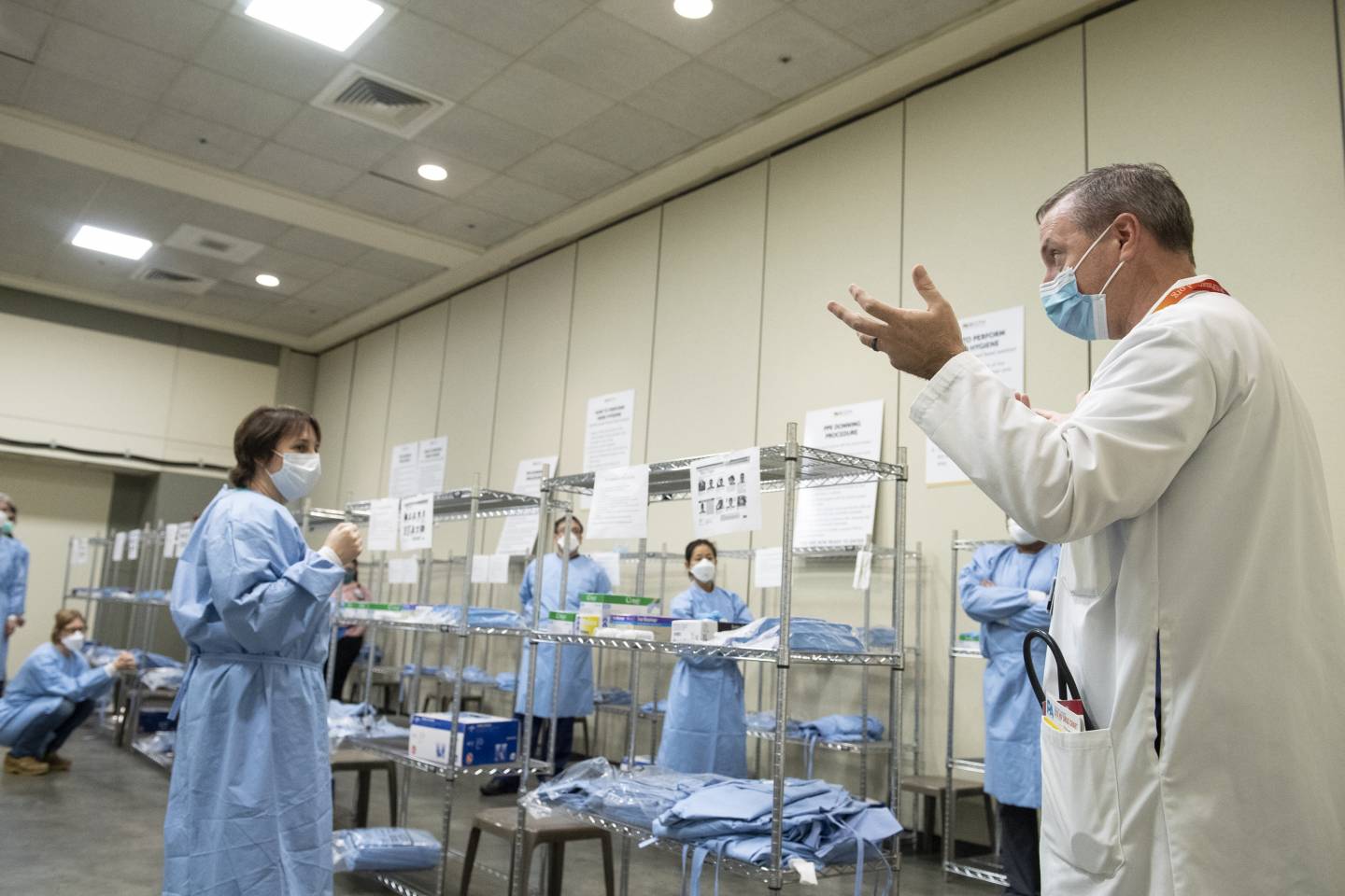 A man leads a group of nurses as they put on gowns