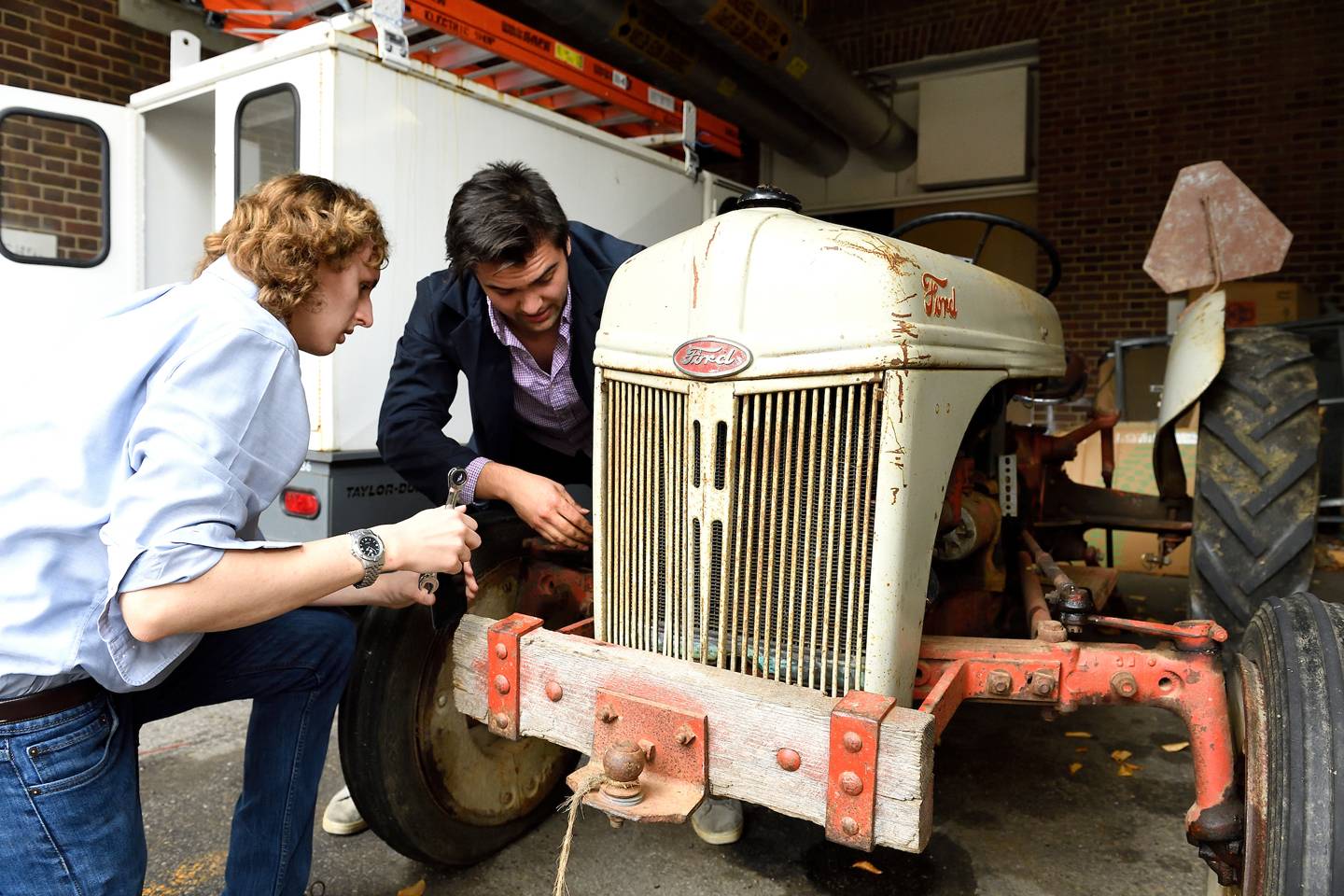 Two students work on a tractor outdoors Two students work on a tractor outdoors