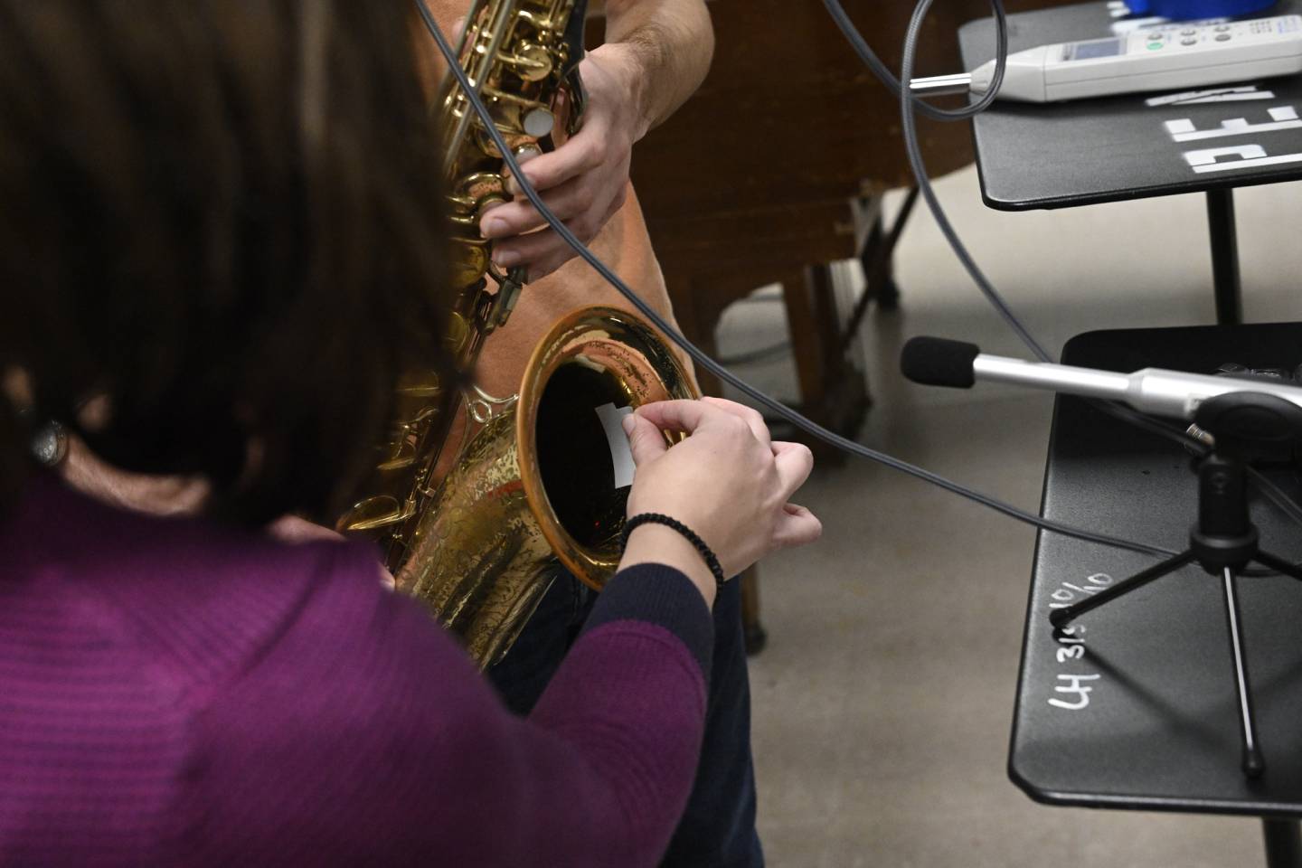 A student attaches a recording device to the bell of a saxophone