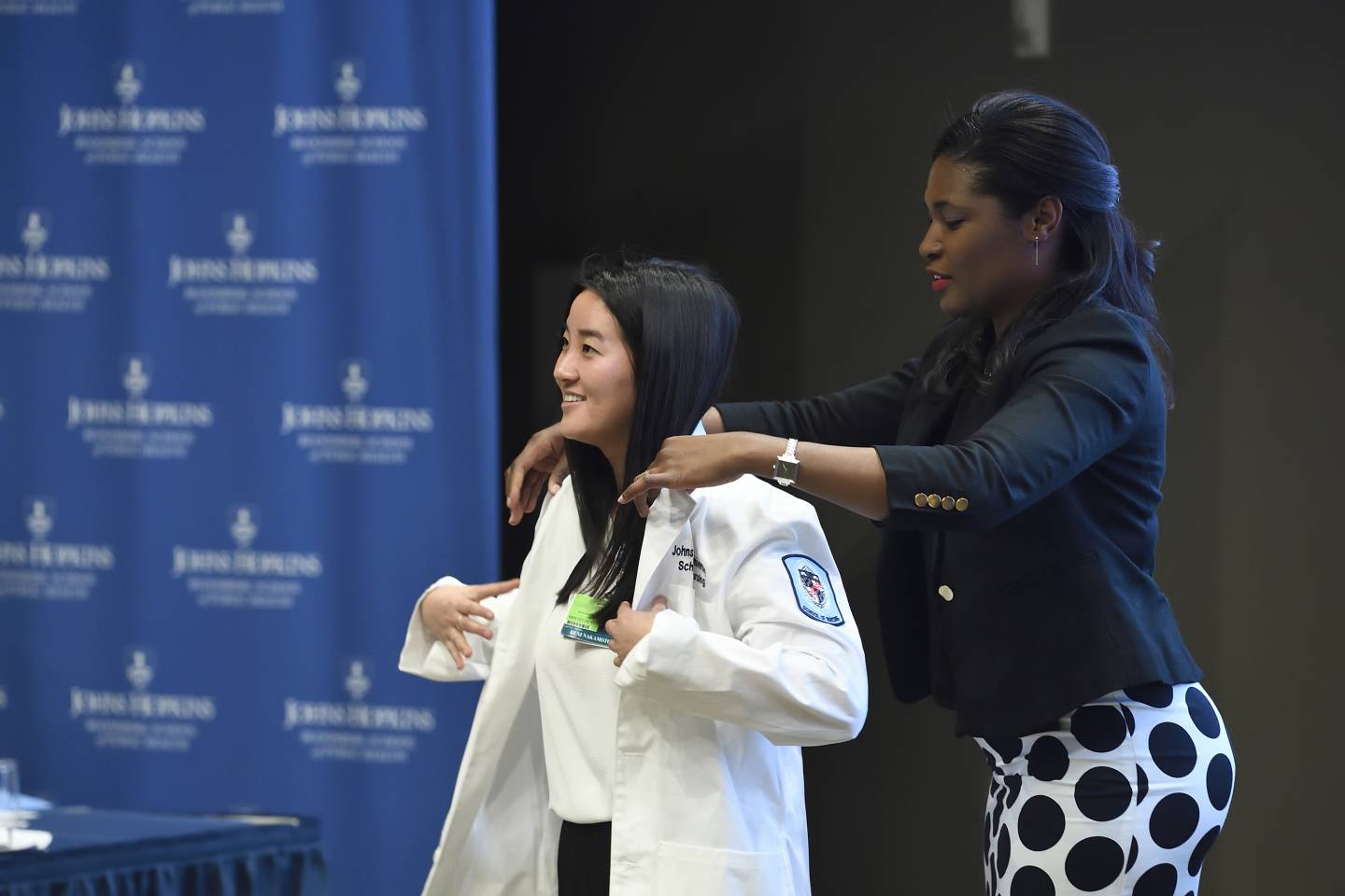 A woman helps a student into her white coat