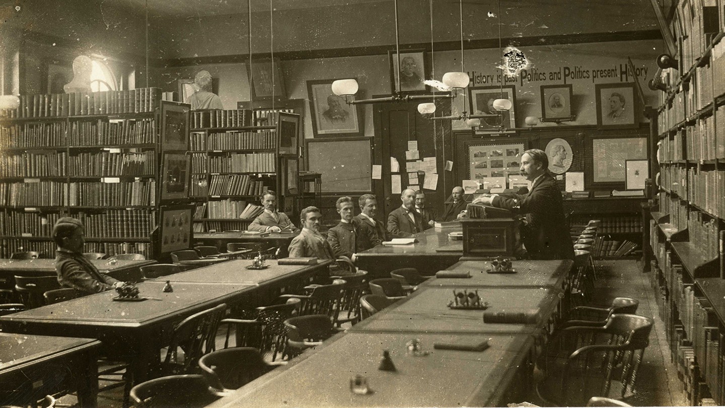 A group of men sit in a seminar room A group of men sit in a seminar room