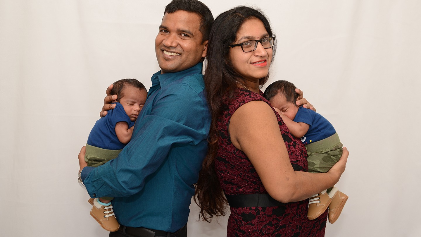 Couple poses back to back for photo with their twin infants Couple poses back to back for photo with their twin infants