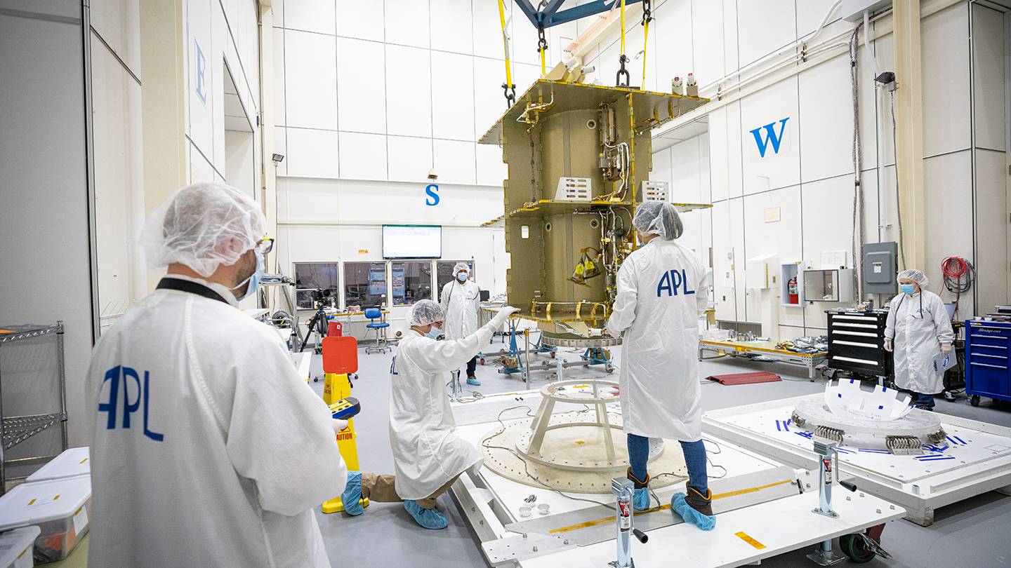 People in masks, lab coats, and booties unpack a spacecraft