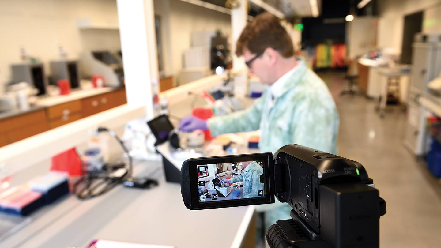 A man in a laboratory records himself with a camcorder