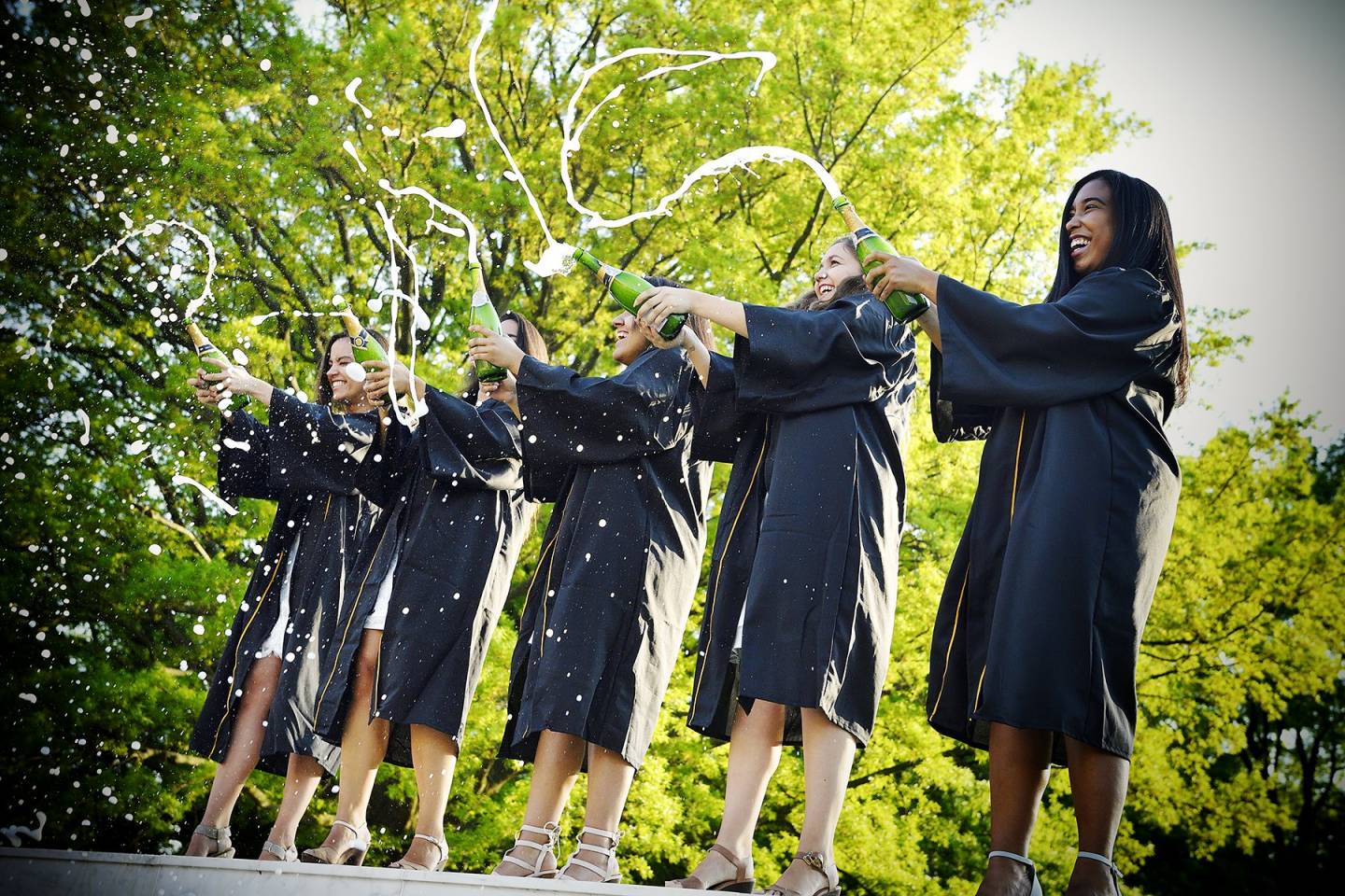 Graduates in caps and gowns spray champagne