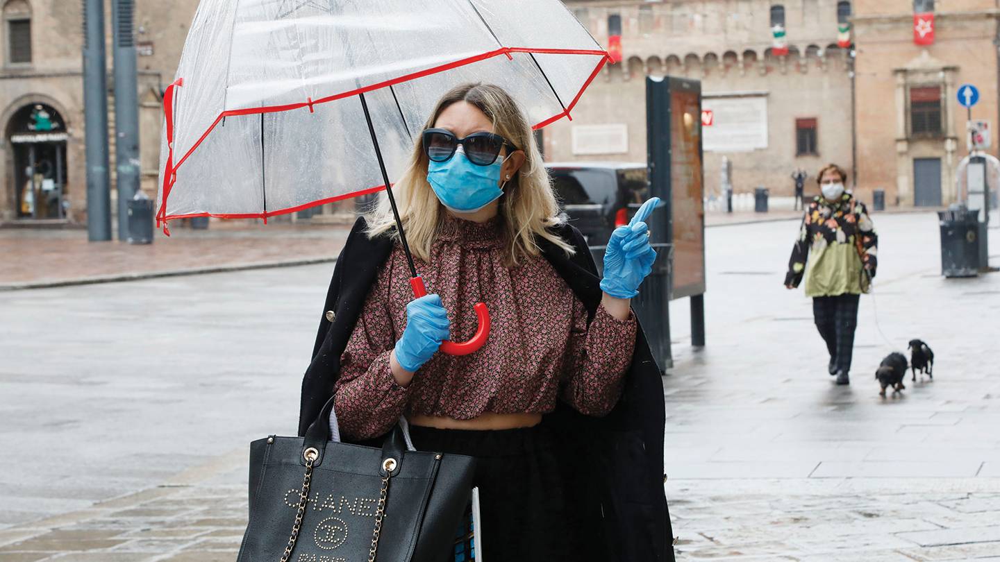A woman with a designer handbag wears surgical gloves and a mask