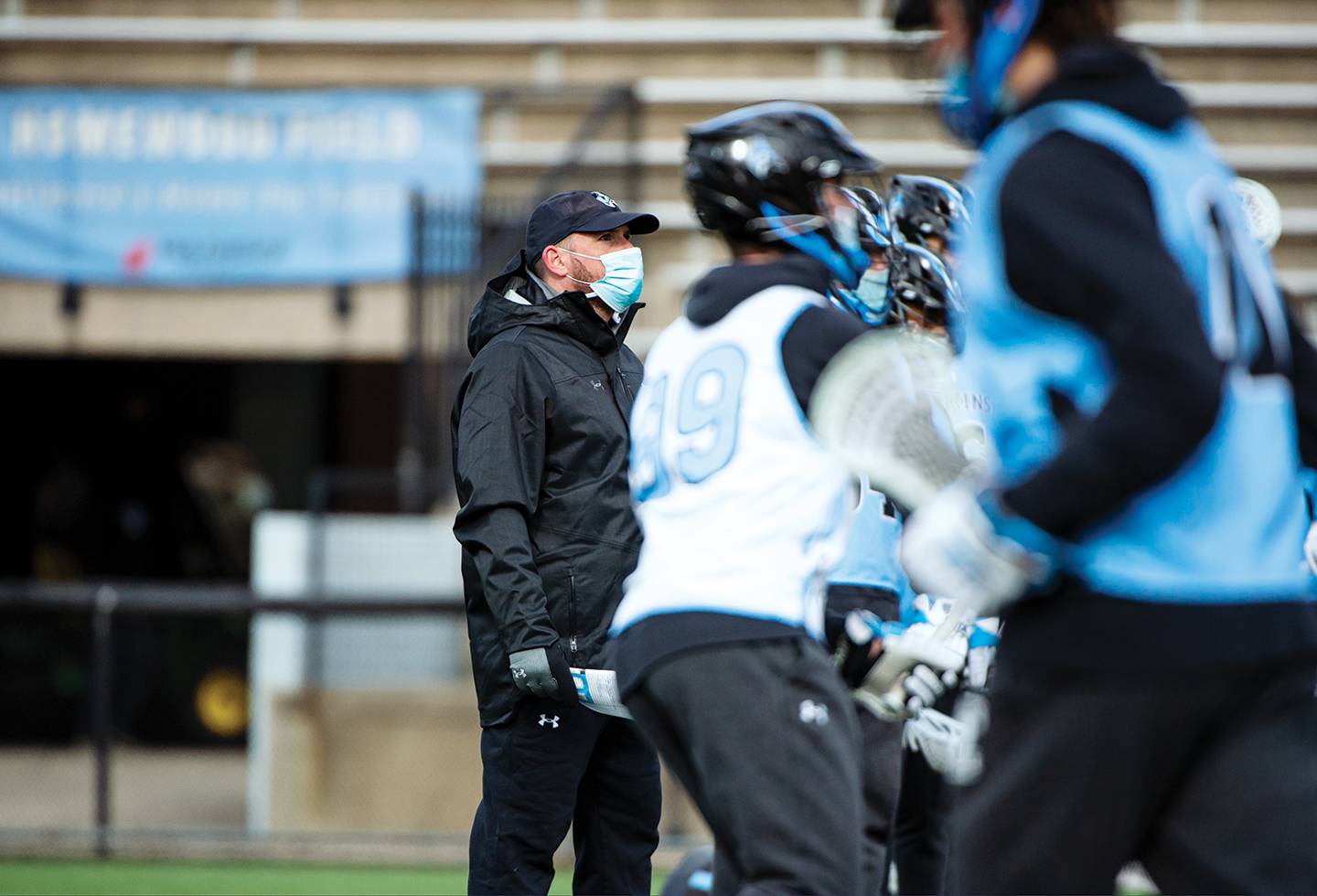 Coach Pete Milliman, wearing a face mask, watches lacrosse practice
